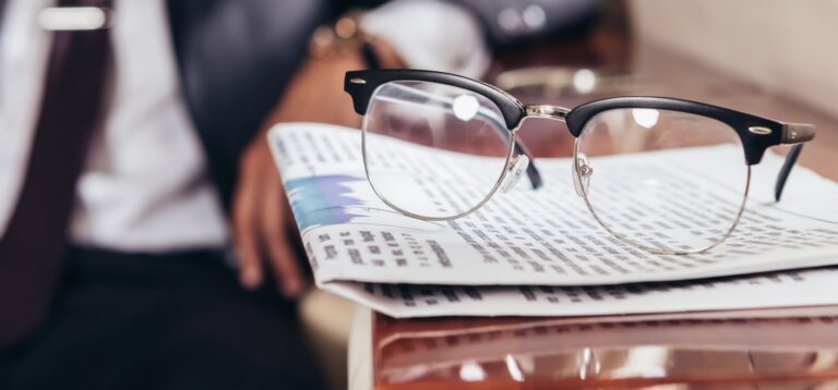 news paper and glasses with businessman in background